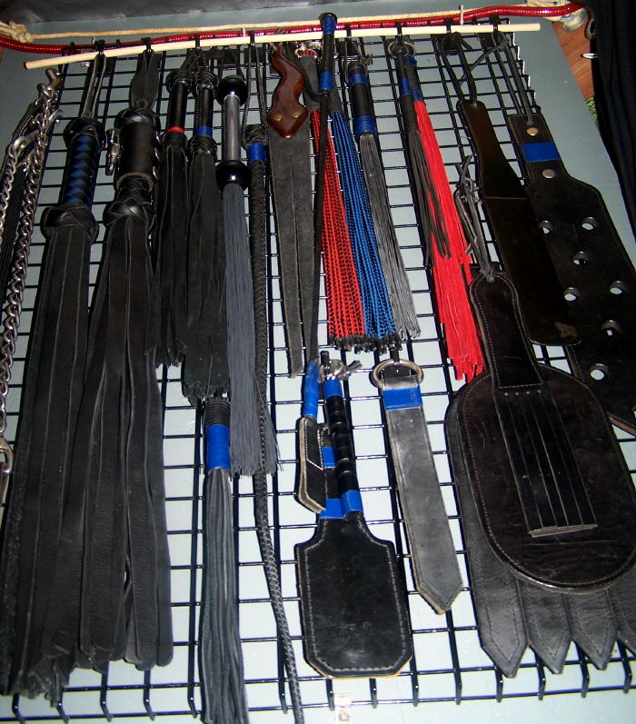 Toy shelf loaded with floggers, whips, tit clamps, cuffs, weights, paddles, restraints, blind folds and more.